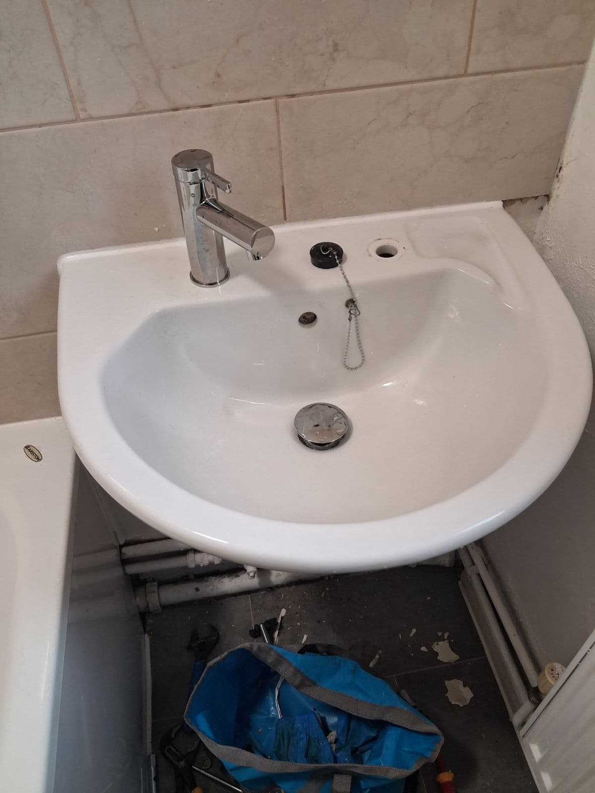 A white pedestal basin with a single chrome mixer tap against a tiled wall