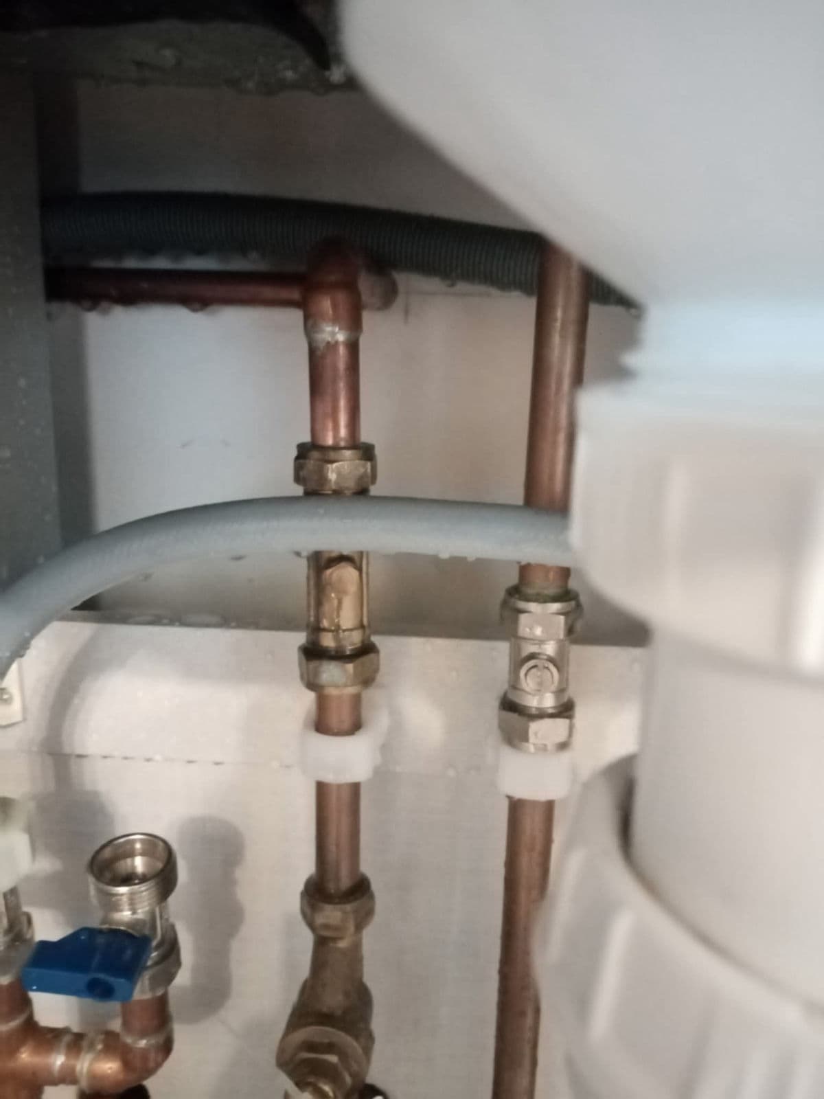 Copper pipes with brass valves and a blue-handled valve under a sink