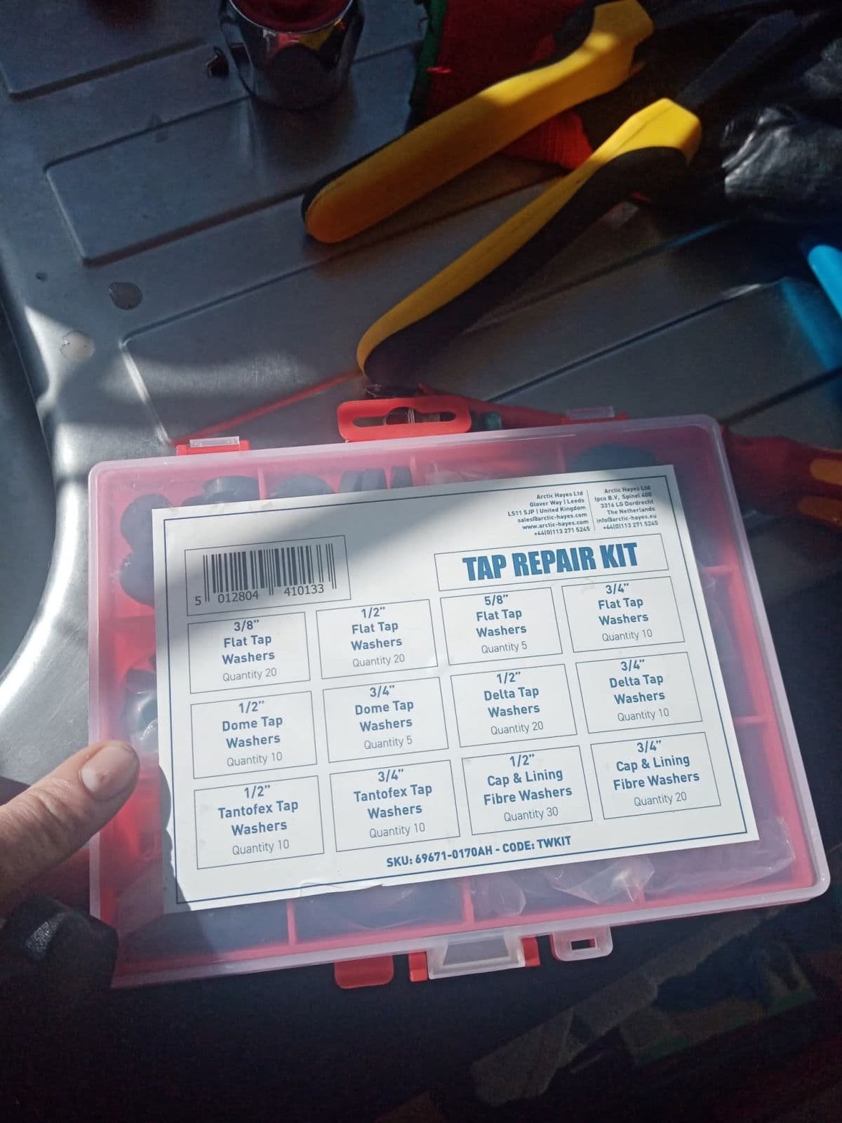 A red tap repair kit box of washers held over a worktop, with pliers