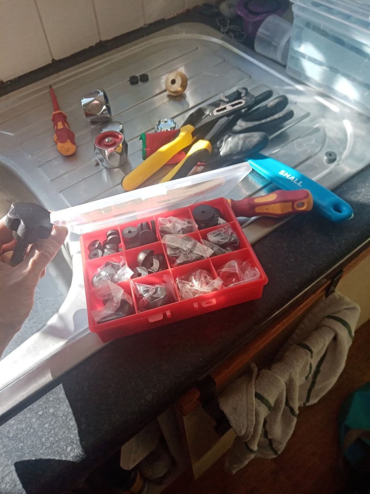 Plumbing tools, gloves and a washer kit laid out on a stainless drainer