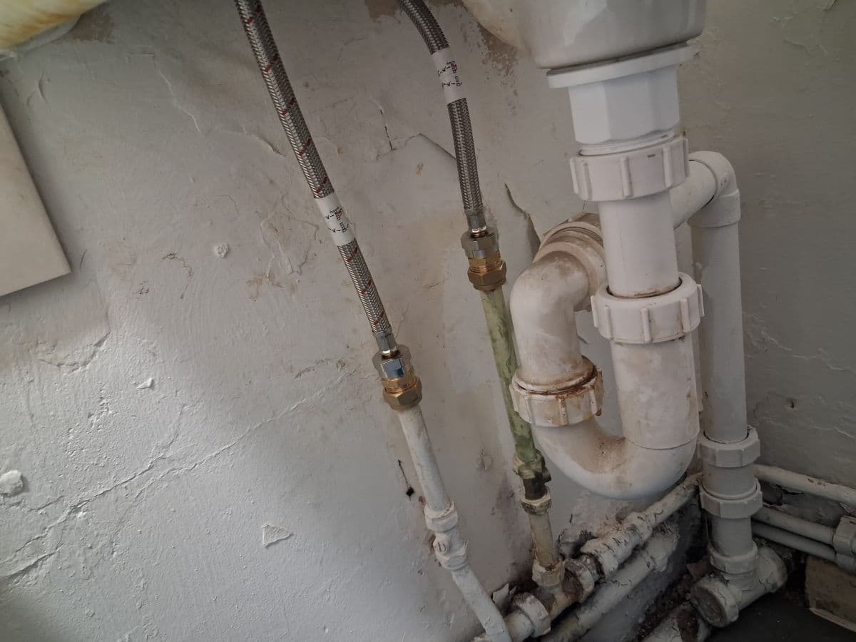 Under-basin pipework: a white waste trap, flexible tap tails and isolation valves