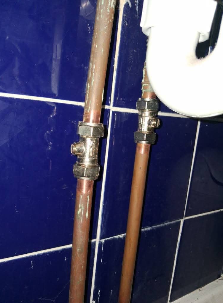 Two copper pipes with brass valves on dark navy tiles