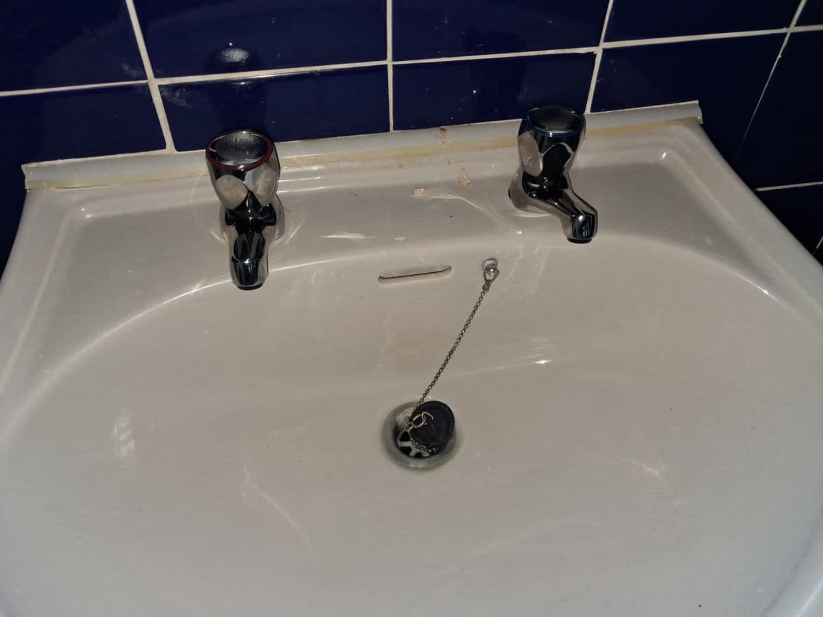 A white basin with two chrome pillar taps on navy tiles